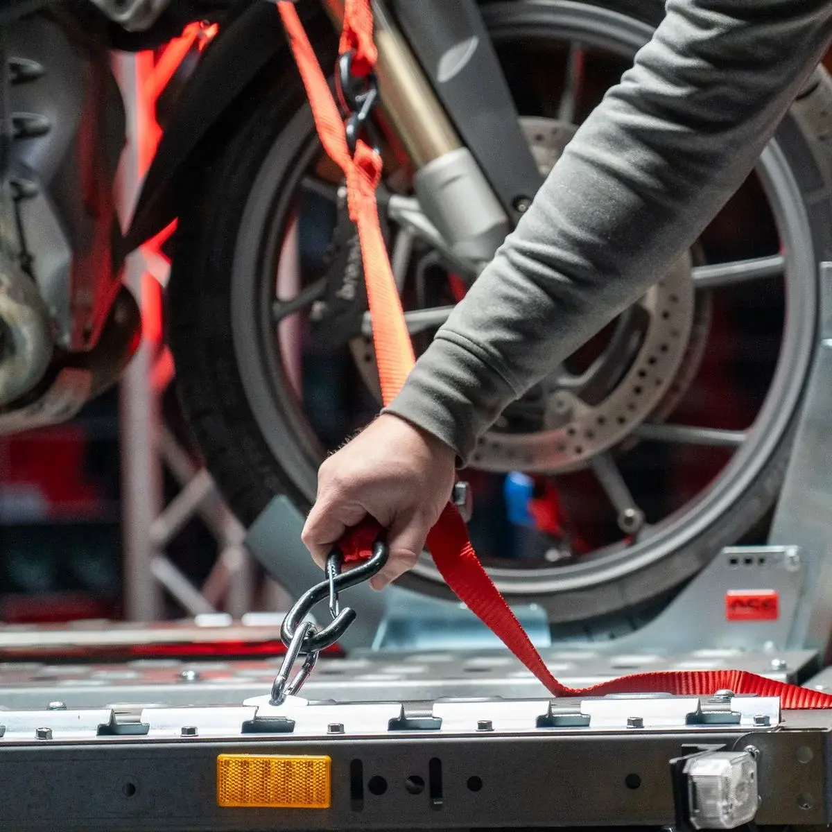 Primer plano de mano asegurando una motocicleta con cinchas rojas en un remolque de transporte.